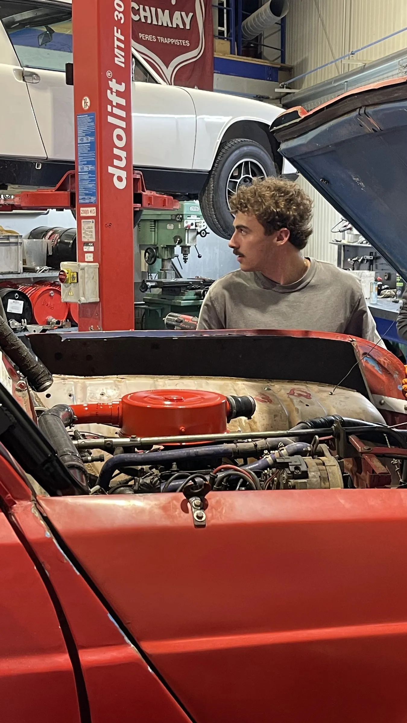 Un membre de l'équipe inspecte le moteur de la 4L, capot ouvert.